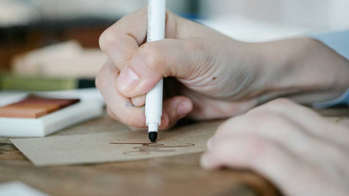 Hand mit Stift die auf einen braunen Blatt schreibt