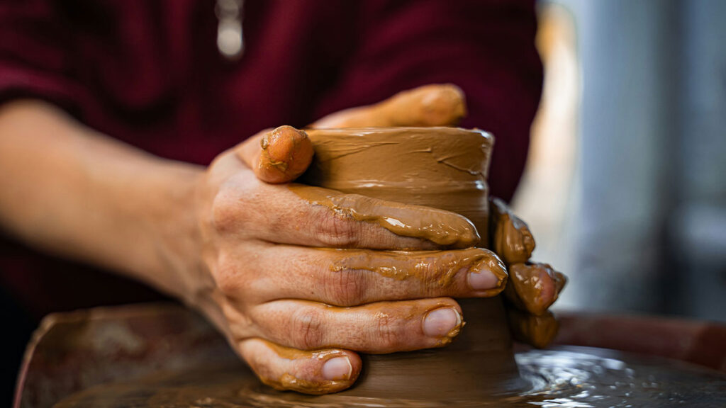 Nahaufnahme von Händen die Ton auf einer Drehscheibe bearbeiten